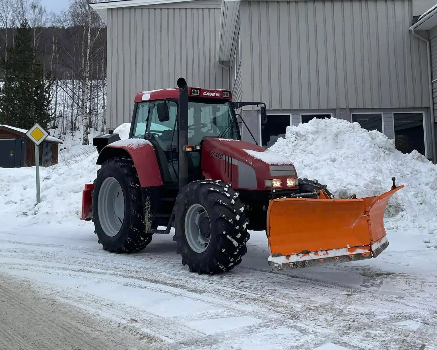 Rød traktor med snøplog for brøyting av snø